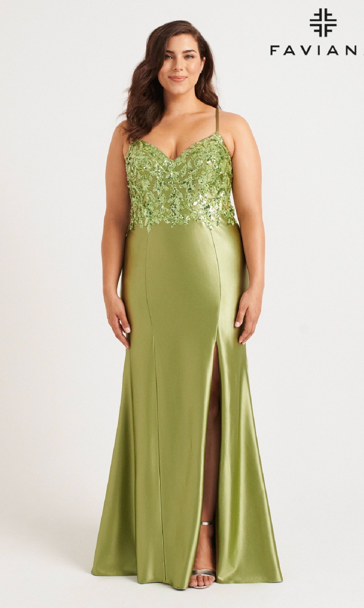 A woman stands against a plain background with the Faviana logo, modeling the Long Plus-Size Prom Dress Faviana 9563—a light green satin gown featuring a sequin applique bodice, thin straps, and a front slit.